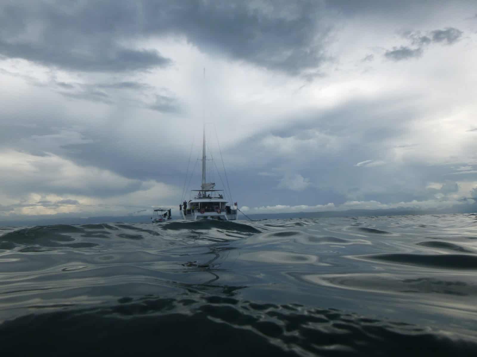 Deep Sea Fishing: A Beginners Guide To Techniques &Amp; Gear 14 a boat floating on top of a body of water under a cloudy sky. the passengers are deep sea fishing